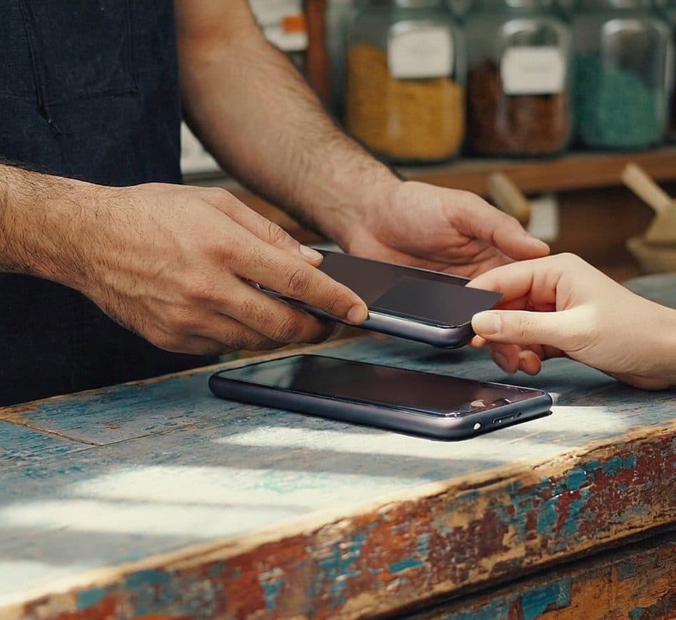 A card held to the back of a phone across a shop counter